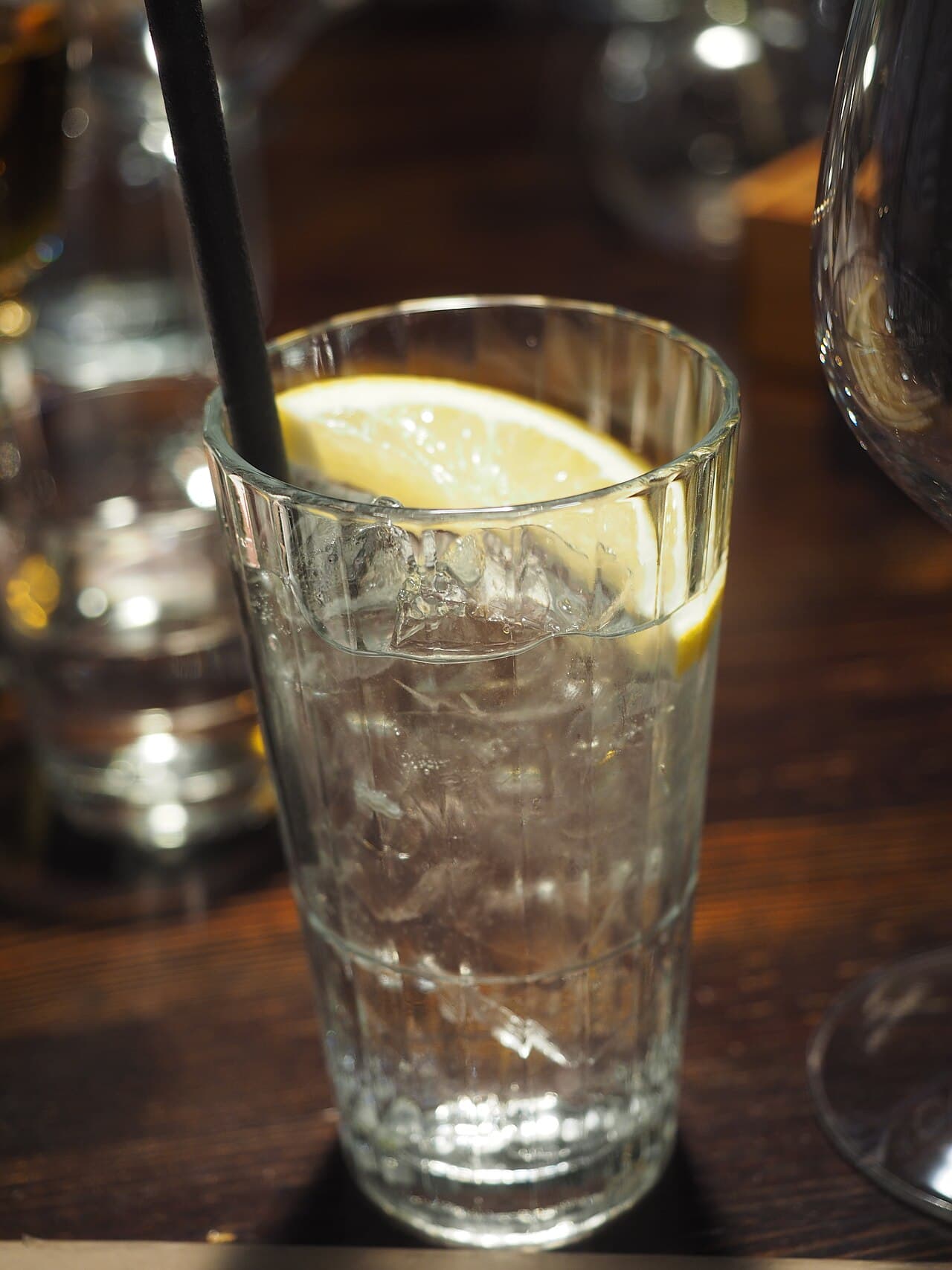 Gin Tonic mit Eis und einer Zitronenscheibe in einem geriffelten Glas auf einem dunklen Holztisch